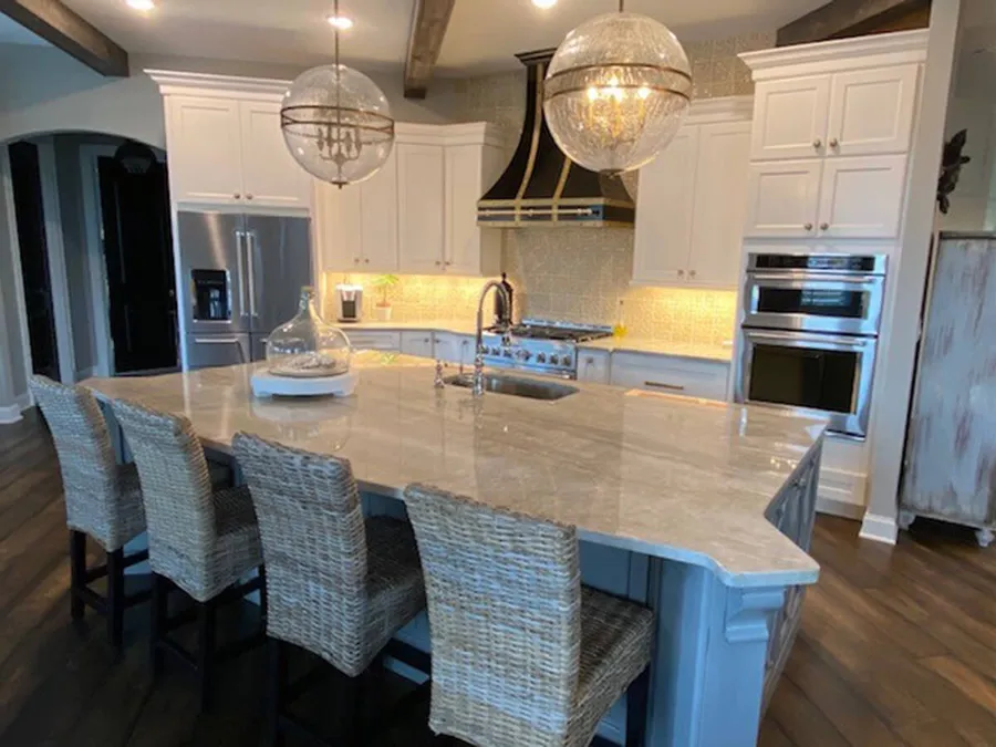 White kitchen with large stone-top island, woven bar stools and globe pendants