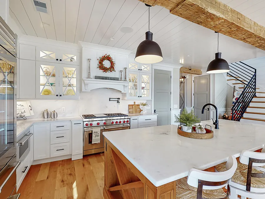 White farmhouse kitchen with marble island, wood beam ceiling and black pendant lights