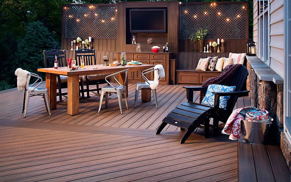 Composite deck at dusk with a dining table, Adirondack chair and string-lit privacy screens