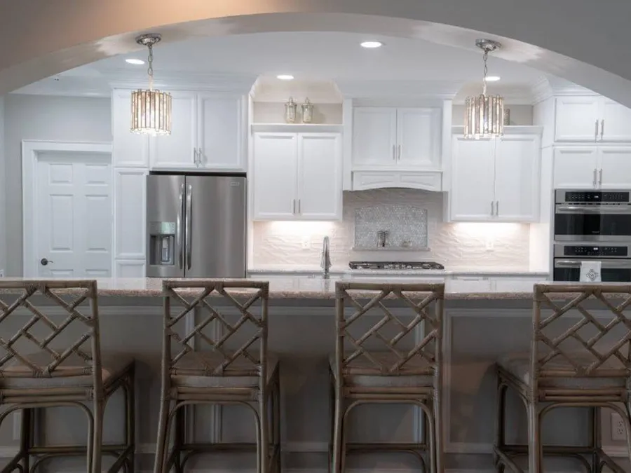 White kitchen seen through an archway with crystal pendants and lattice-back bar stools