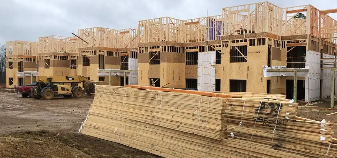 Multi-story wood-framed townhomes under construction with lumber stacked in front