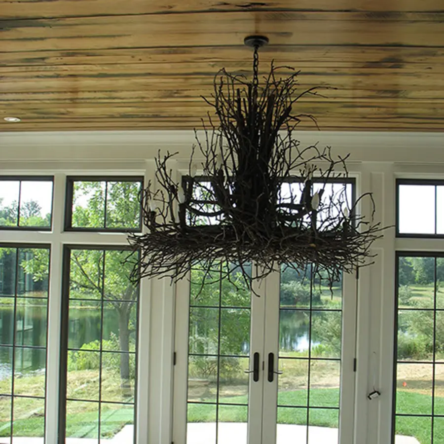Twig chandelier under a plank wood ceiling in a sunroom overlooking a pond