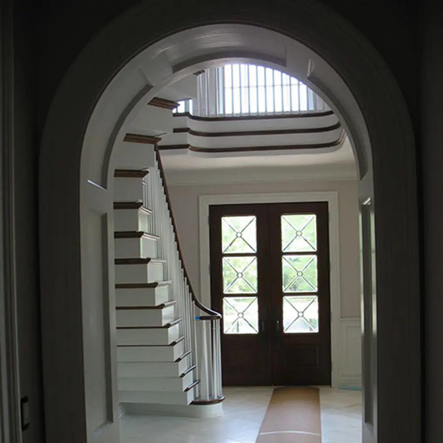 Arched opening framing a foyer with a curved staircase and double entry doors