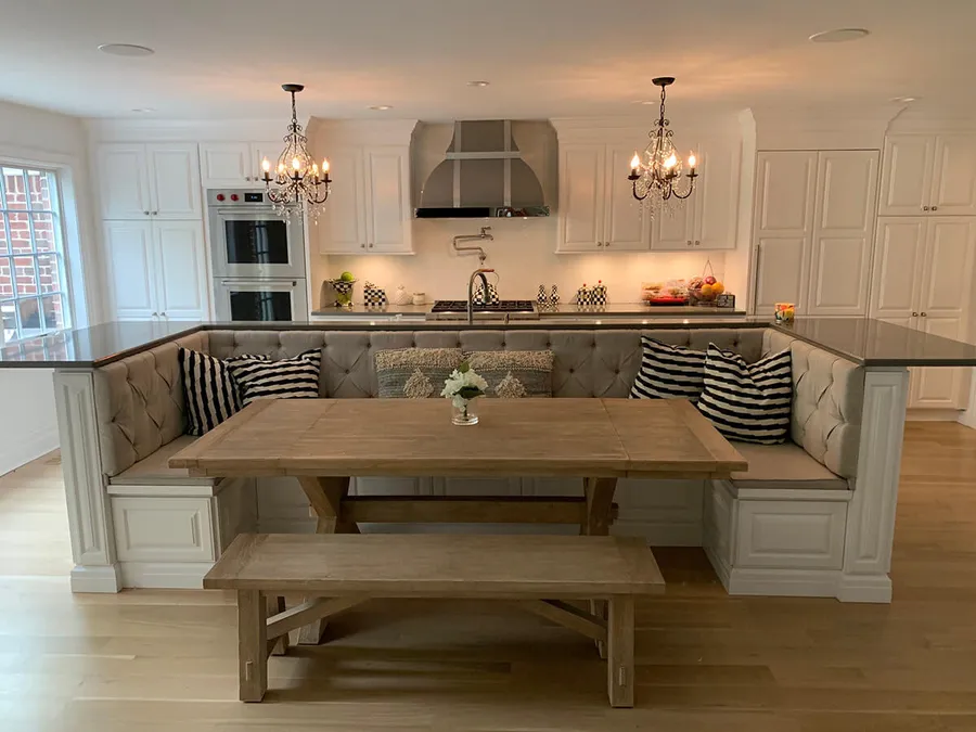 White kitchen island with built-in tufted bench seating around a wood dining table