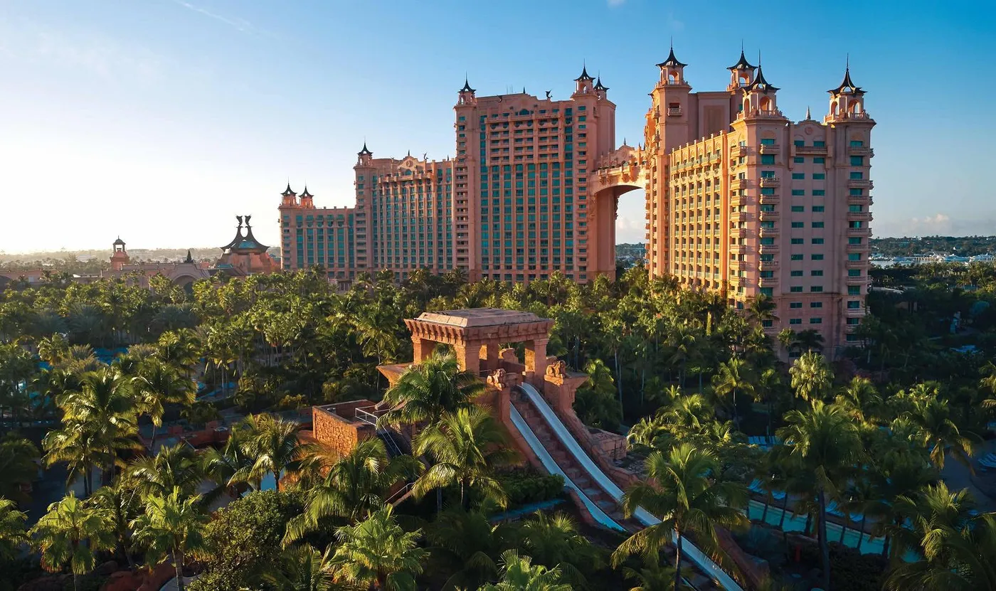 Pink resort towers joined by an arched bridge above palms and water slides