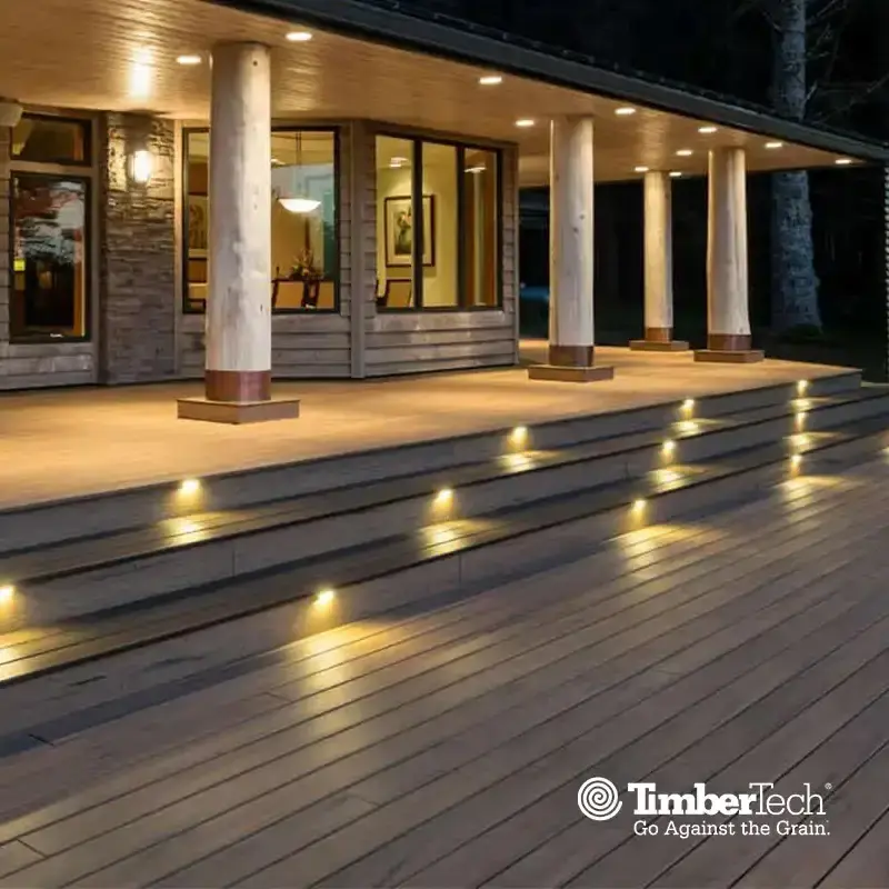 Composite deck with lit stair risers at dusk, with a TimberTech logo