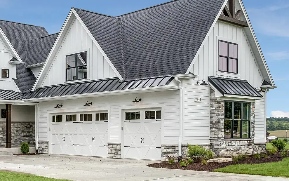 White farmhouse-style home with attached garage, carriage-style doors and metal roof accents