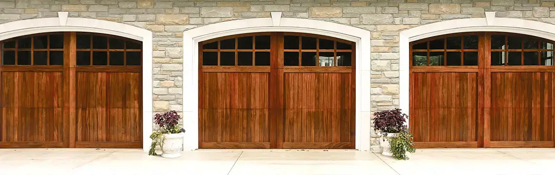 Three arched wood garage doors with window lites set in a stone wall