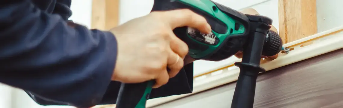 Close-up of a hand using a power drill to fasten trim during siding installation