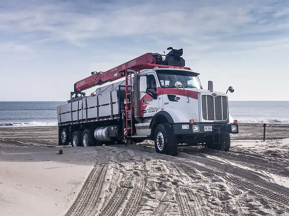 Red and white delivery truck with a knuckle-boom crane driving on a sandy beach