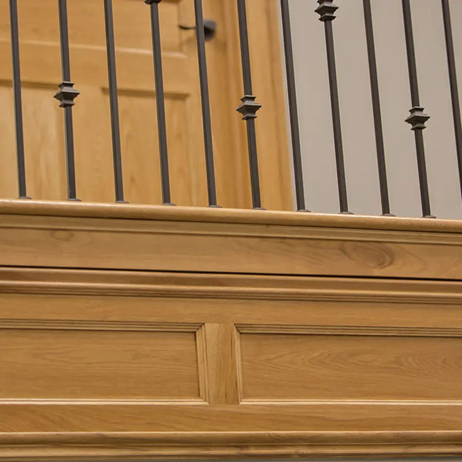Close-up of a stained wood stair balcony with raised panels and iron balusters