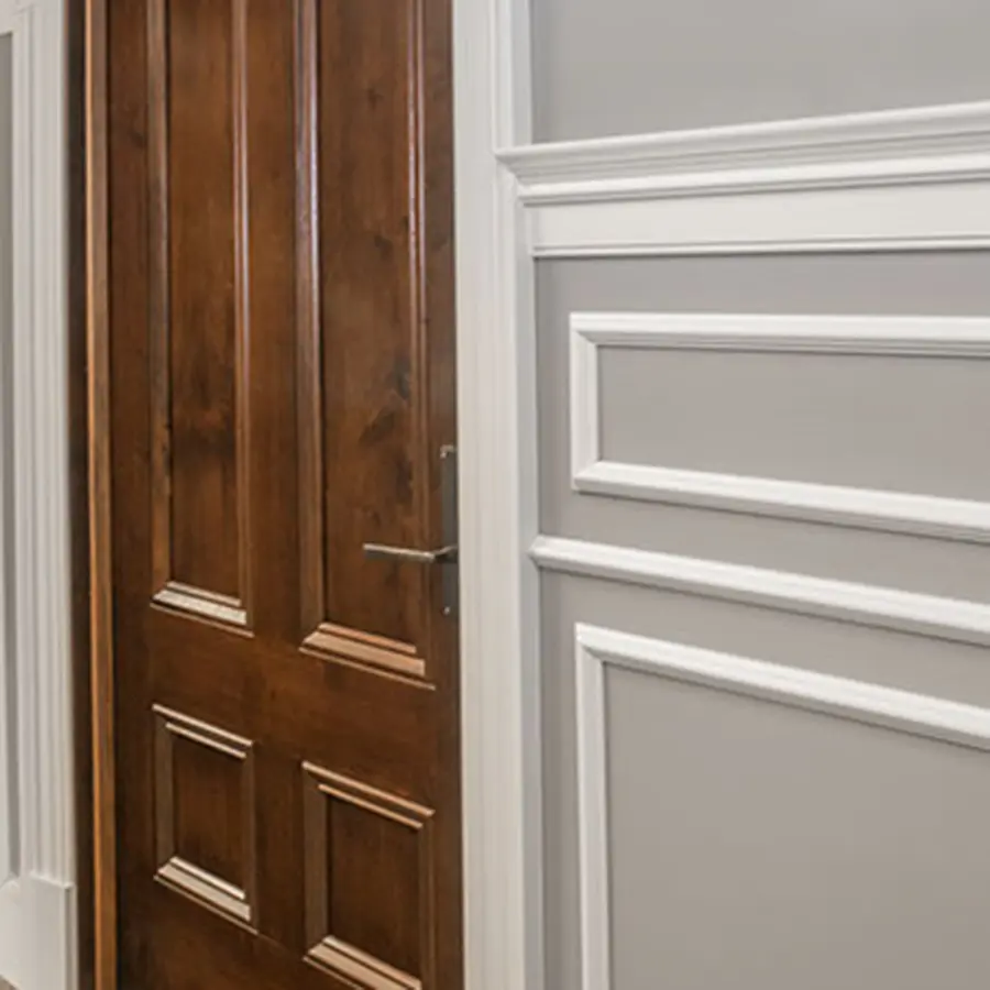 Stained wood paneled door beside gray wainscoting with white trim molding