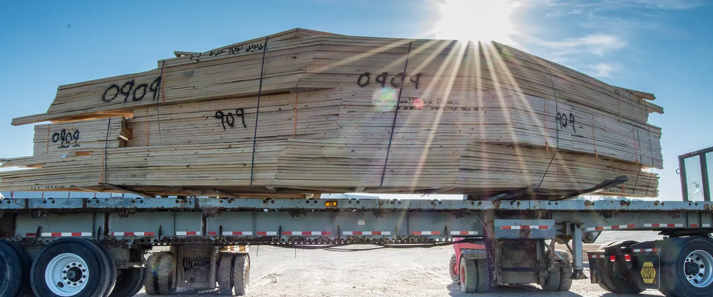 Large banded bundle of lumber on a flatbed trailer against a sunny sky