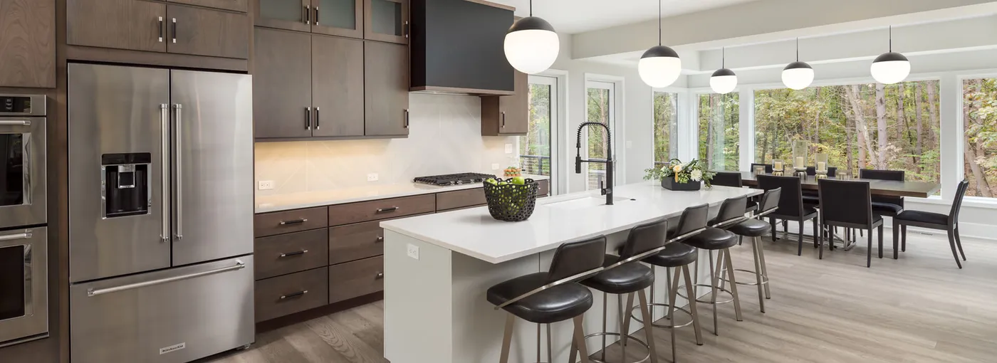 Open kitchen with dark cabinets, white island with bar stools and globe pendants by a dining area