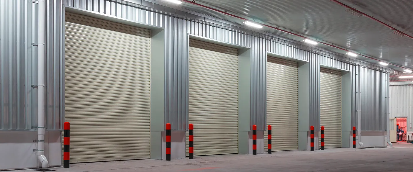 Row of roll-up commercial doors in a metal-clad warehouse with striped bollards