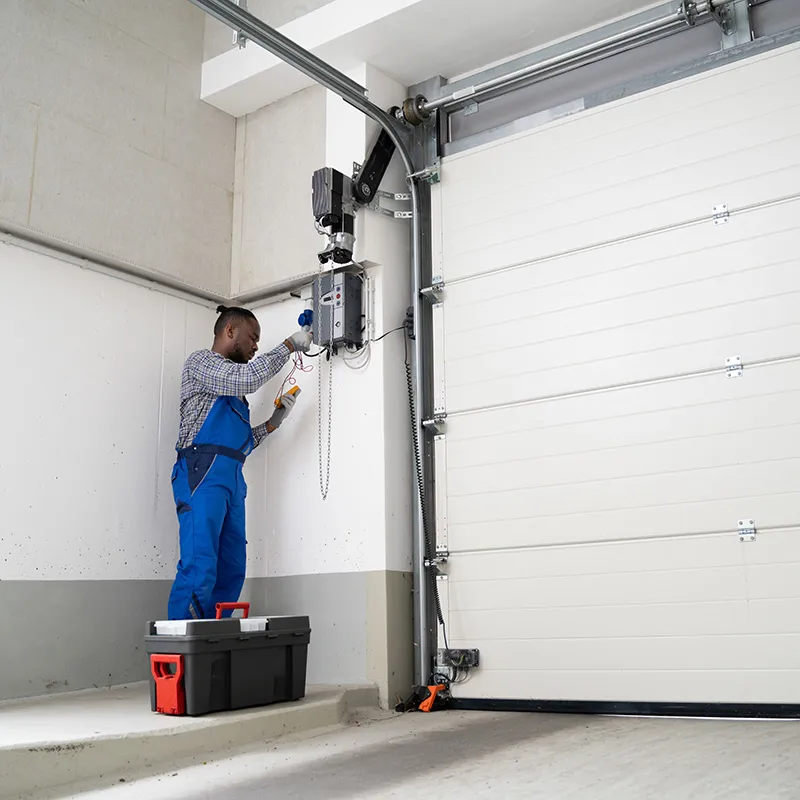Technician in blue overalls servicing the opener on a sectional commercial door