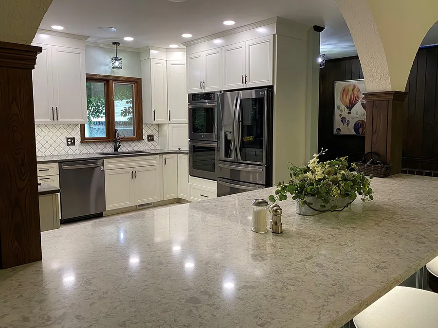 White kitchen with stainless appliances and a large speckled stone peninsula
