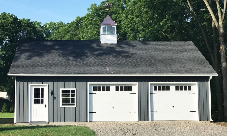 Gray board-and-batten two-car garage with white carriage doors and a cupola
