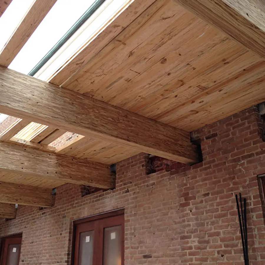 Exposed wood ceiling beams and plank decking over an old brick wall with skylights