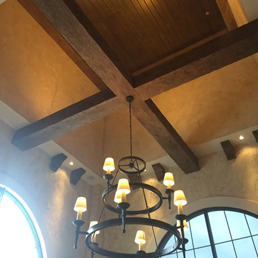 Rustic wood ceiling beams crossing above a two-tier iron chandelier