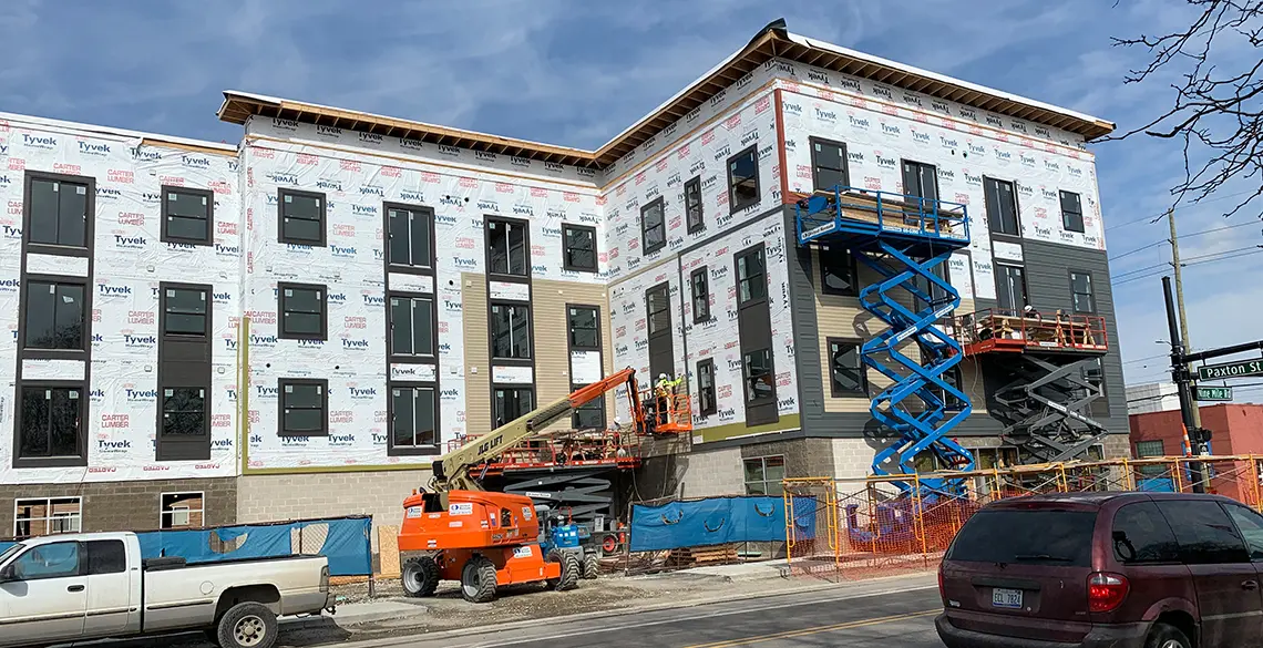Multi-story apartment building in Tyvek wrap with lifts and crew working on site