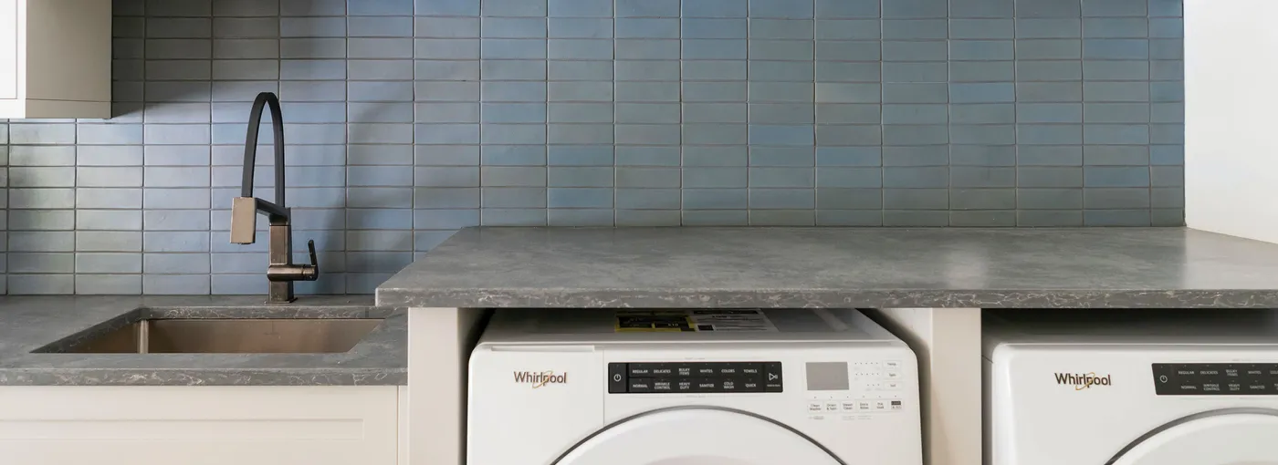 Laundry area with blue tile backsplash, gray countertop, sink and front-load washer and dryer