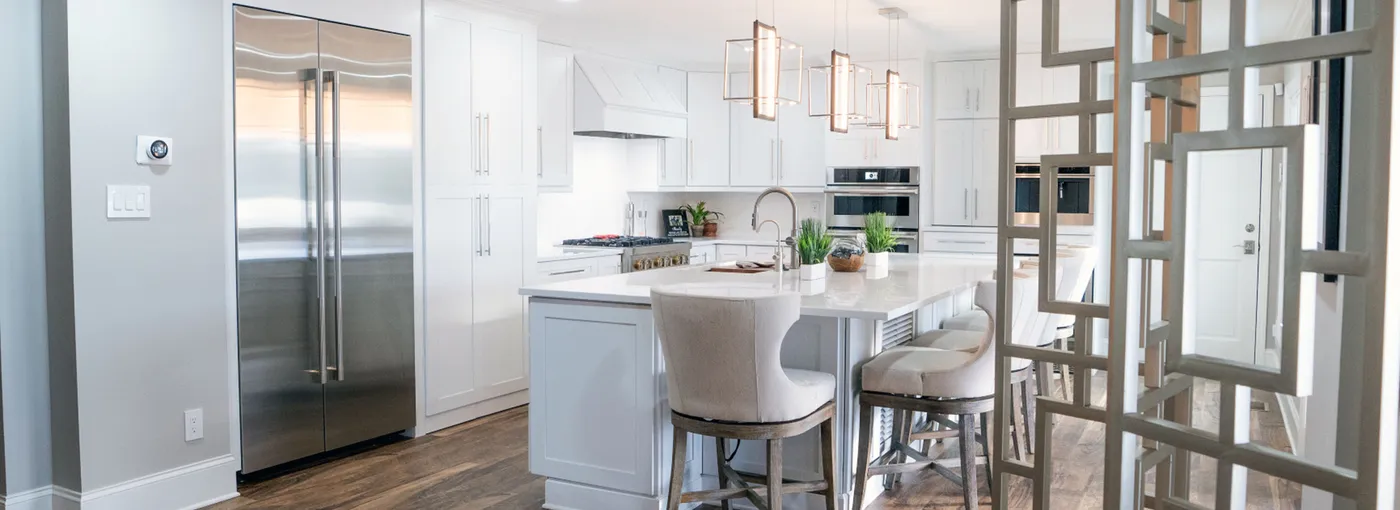 White kitchen with island, upholstered stools and pendant lights seen through a lattice screen