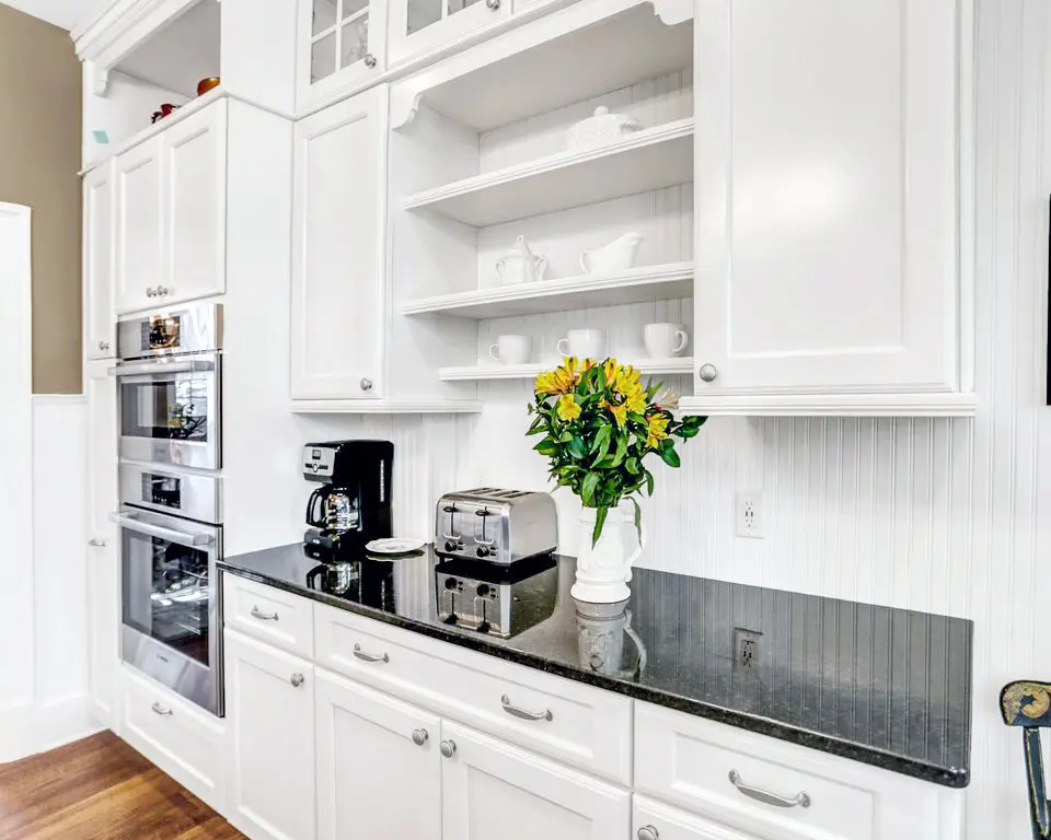White cabinets with open shelves, black countertop, wall ovens and yellow flowers